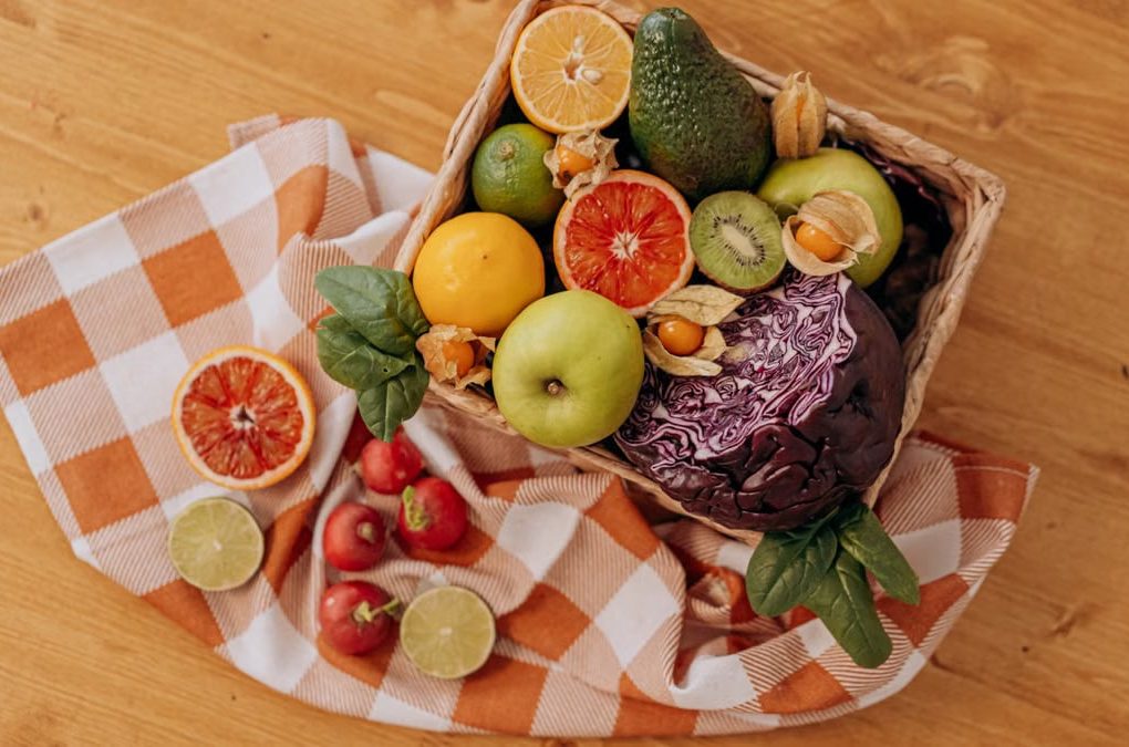 A colorful mix of fruits and vegetables arranged in a basket on a rustic wooden table.